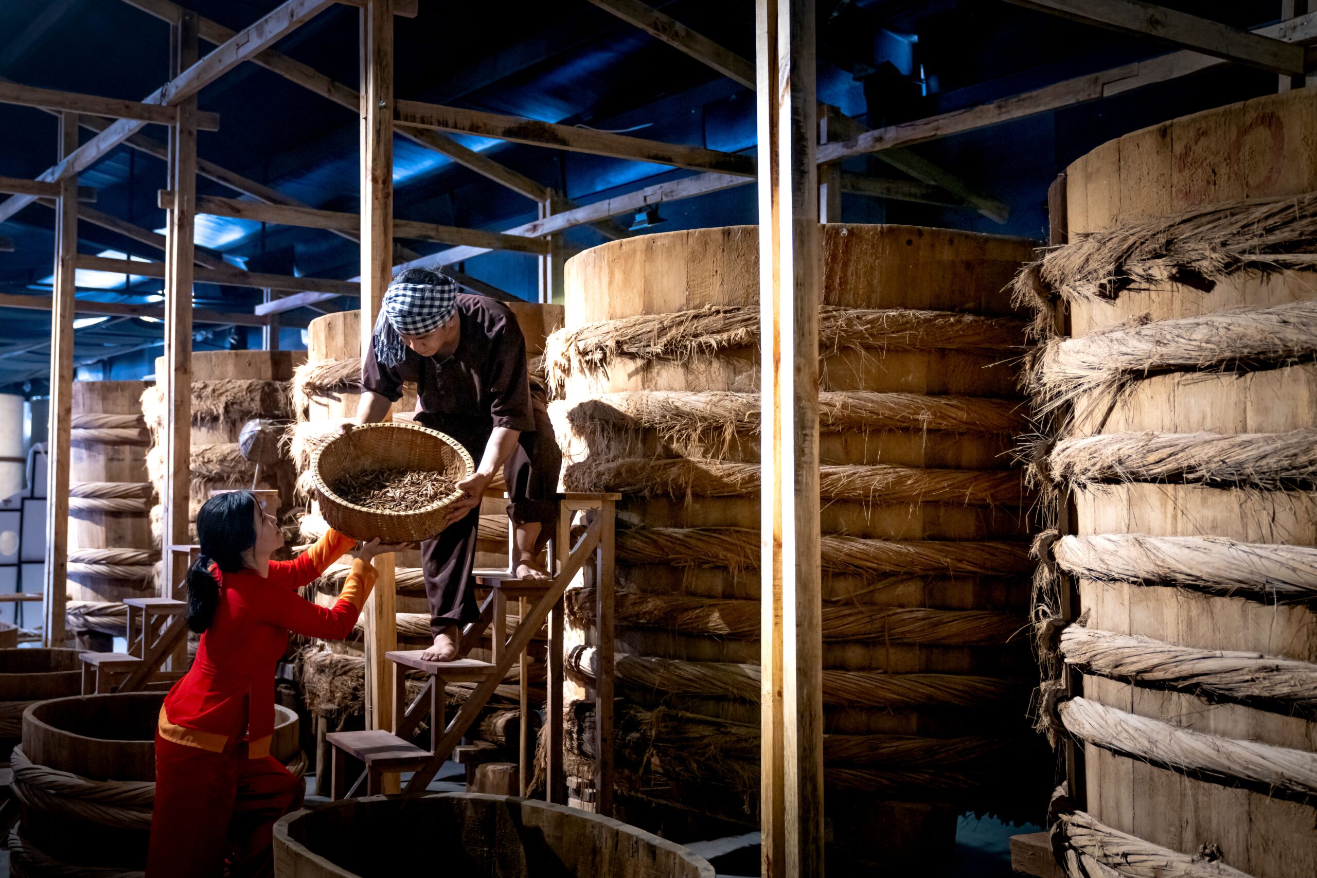Factory employees working in fish sauce manufacture near wooden barrels with ropes