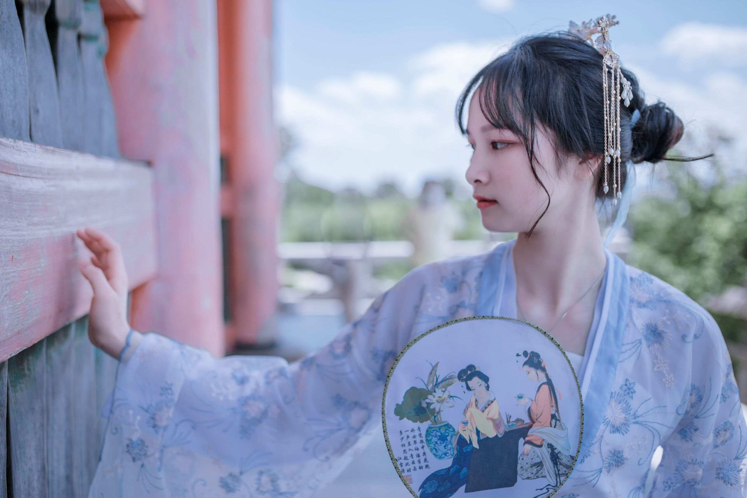 Beautiful woman in traditional hanfu, holding a fan, outdoors.