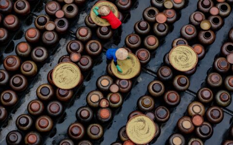Aerial view of workers in colorful attire preparing soy sauce in ceramic jars in Vietnam.