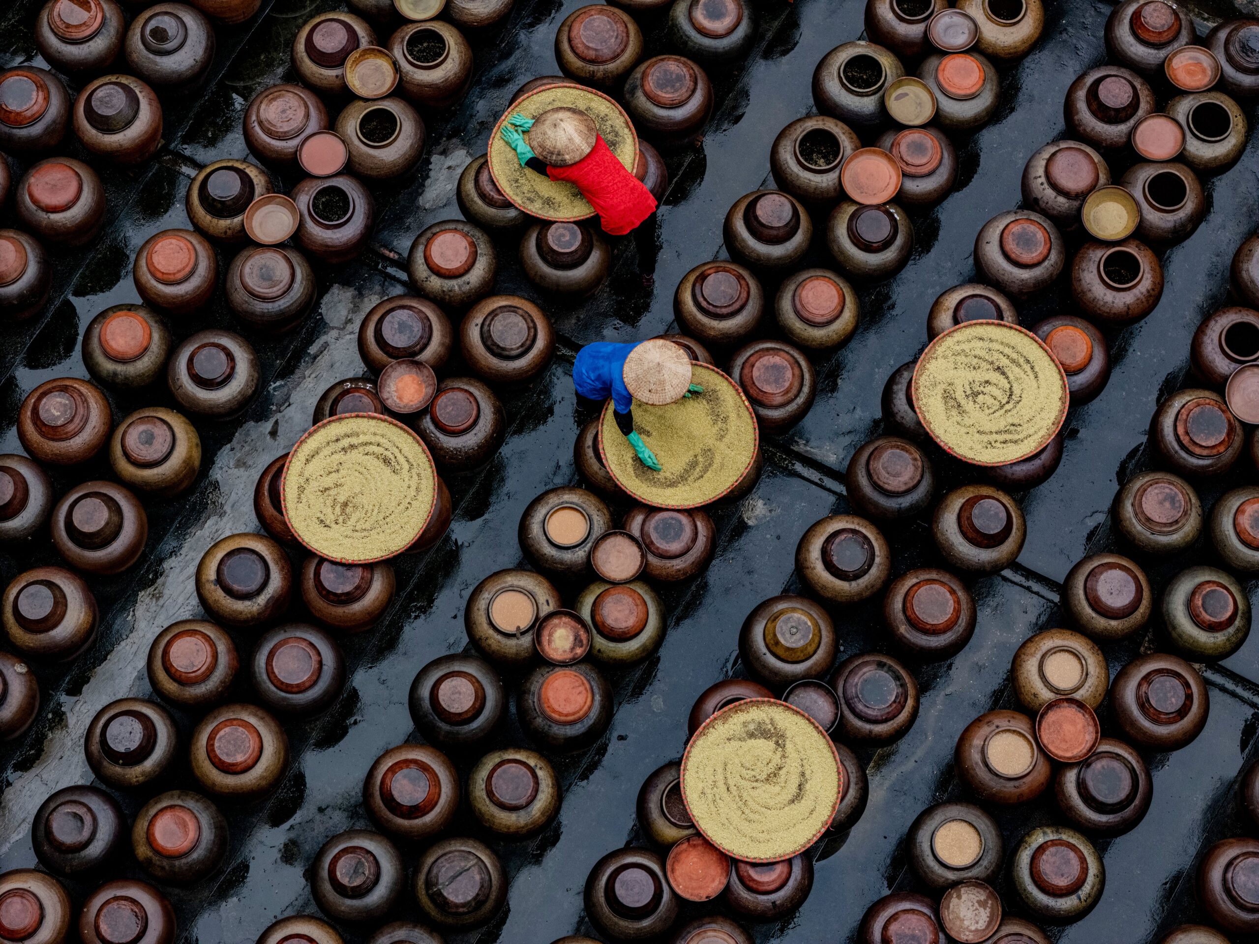 Aerial view of workers in colorful attire preparing soy sauce in ceramic jars in Vietnam.