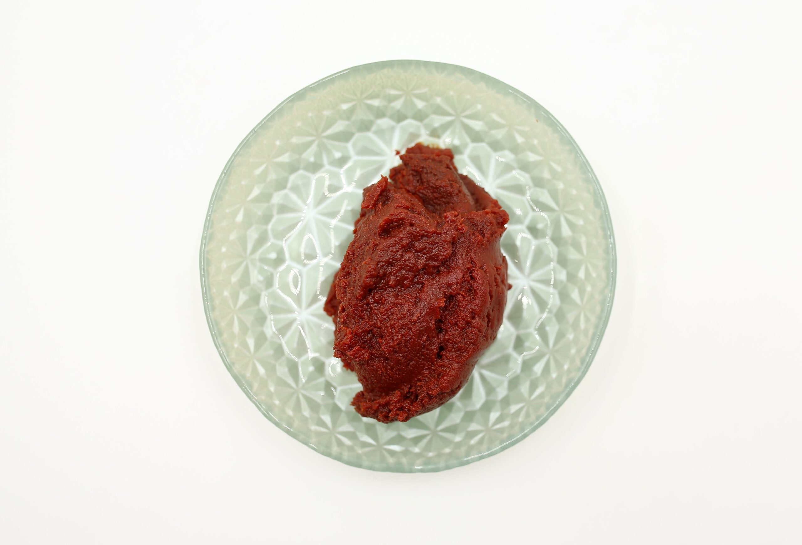 Red paste displayed in a textured glass bowl on a white background, captured overhead.