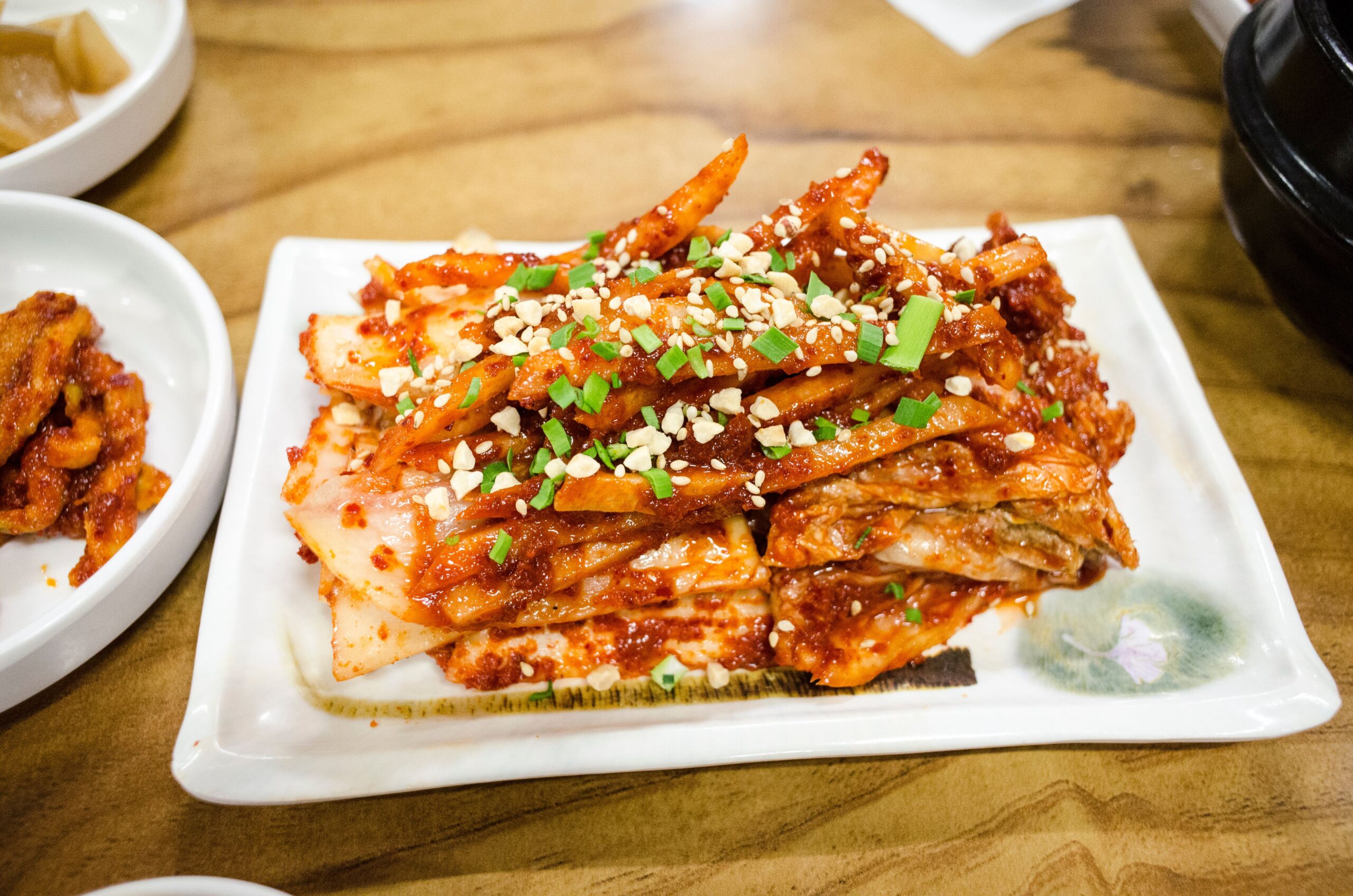 Delicious spicy kimchi served with green onions and nuts on a ceramic plate.