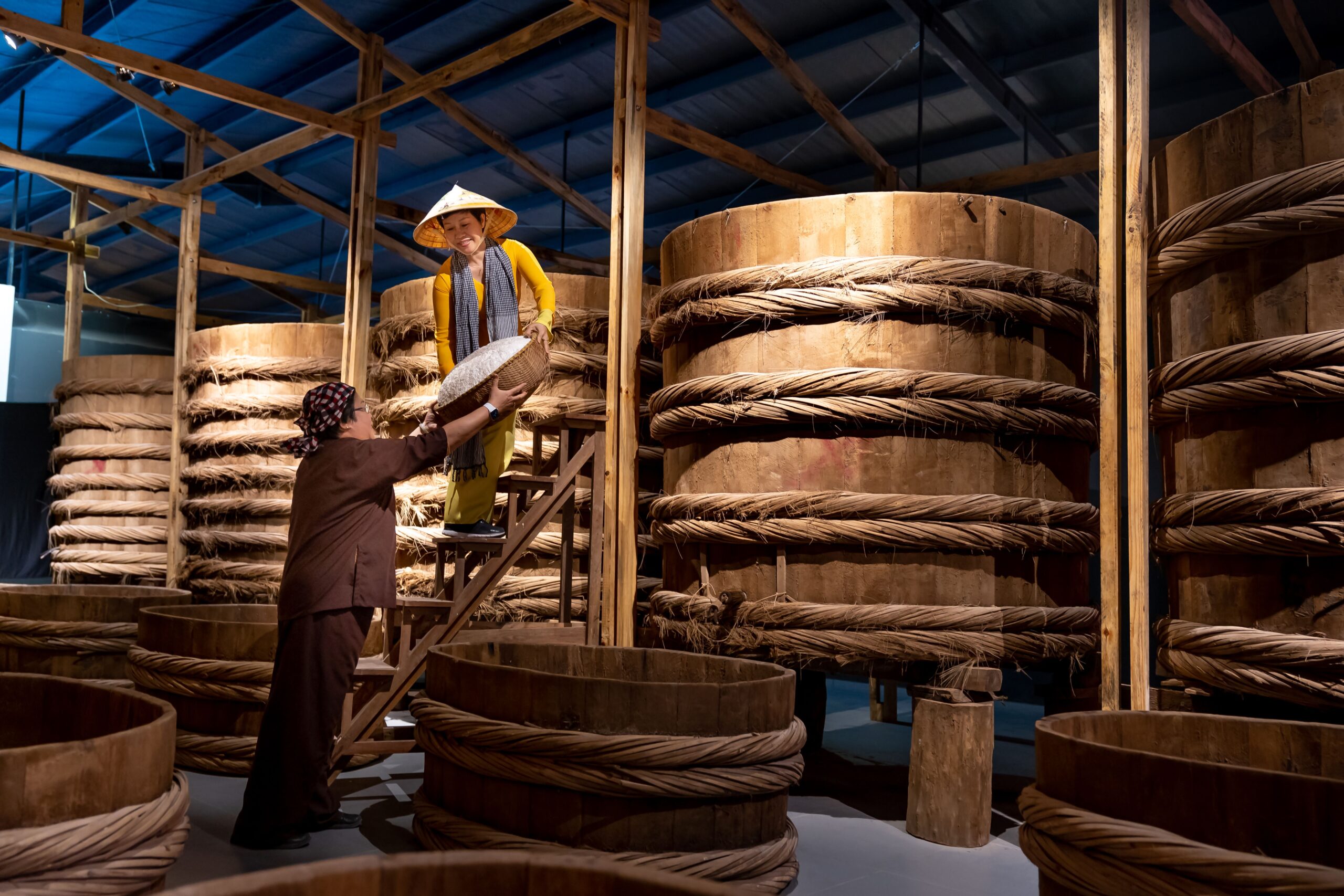 Women making fish sauce using traditional methods with large wooden barrels.
